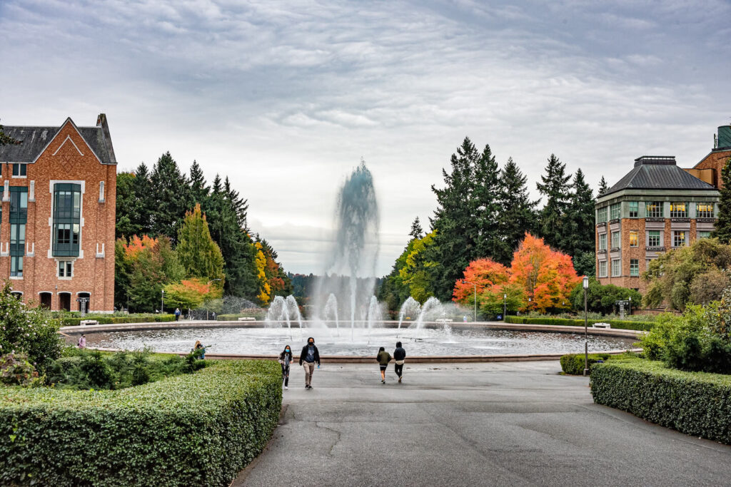 Students walking on the University of Washington campus near a fountain.