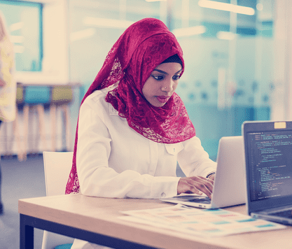 A student sits at a desktop working on a laptop.