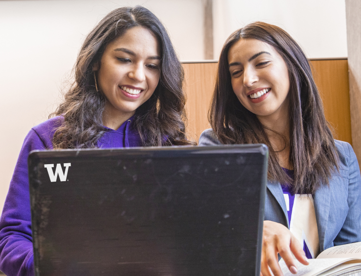 Two students smile while looking at master's in information management project on a laptop.