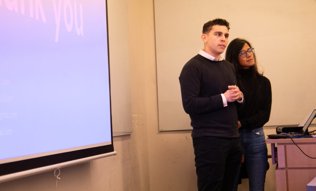 Two students present in front of a projector screen in a classroom.
