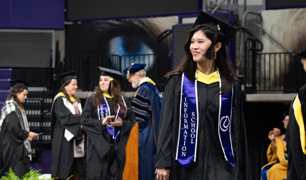 A graduate in cap and gown smiles at someone off-camera.