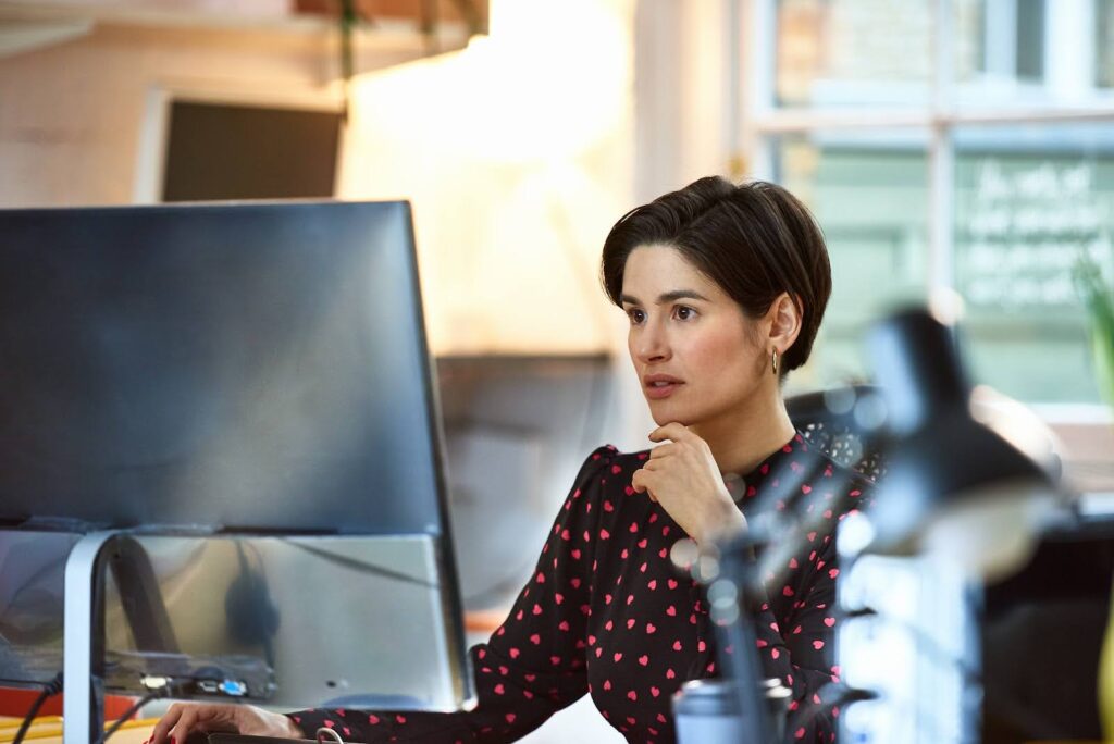 A woman in business attire works at an office computer.