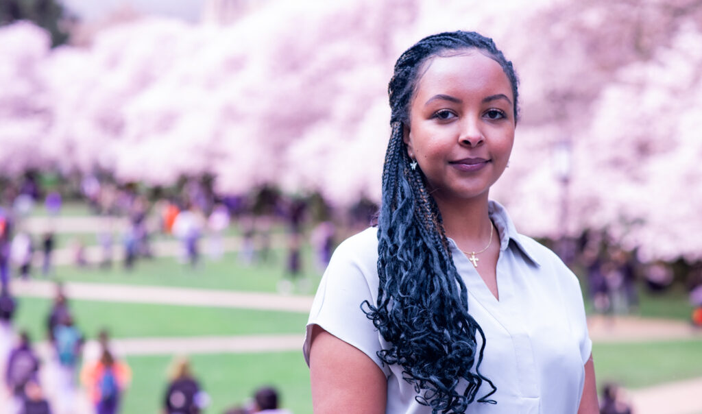 UW MSIM student Afomia Assefa stands in front of a row of trees in full bloom.